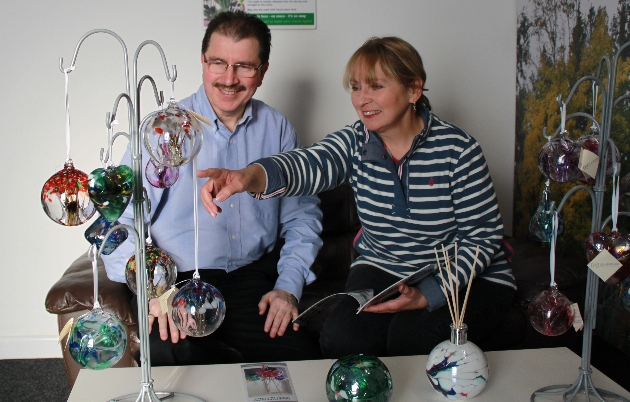 man and woman sitting down pointing at glass baubles hanging on a jewellery tree