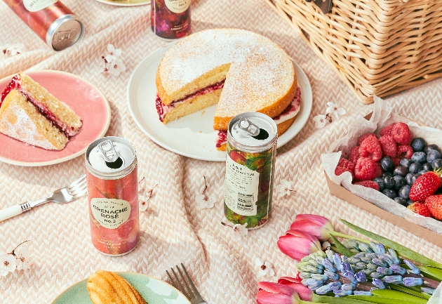 tin wines on a picnic blanket with flowers food and hamper