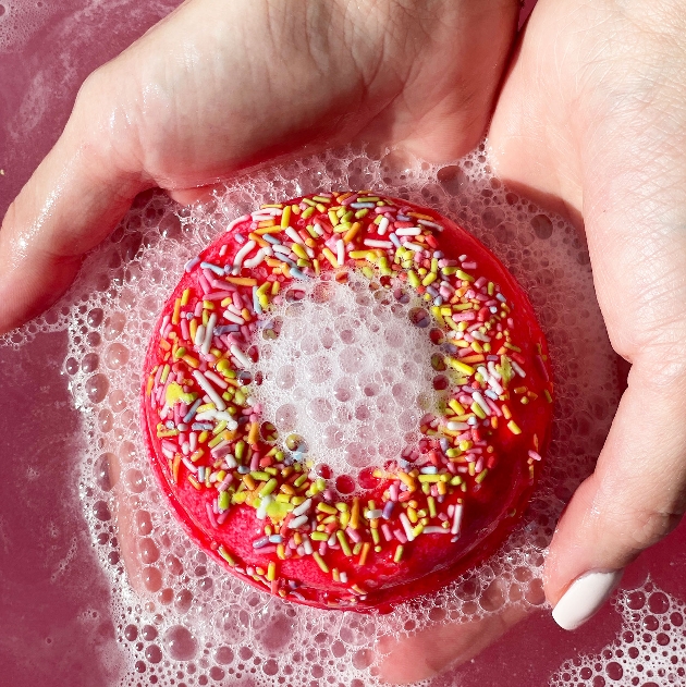 pair of hands holding a doughnut-shaped bath fizzer in water