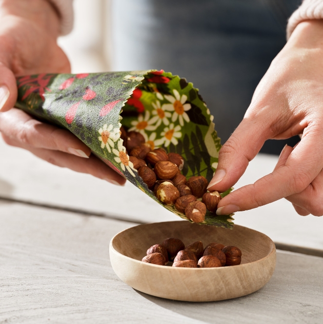 beeswax wrap being used to pour nuts in a bowl