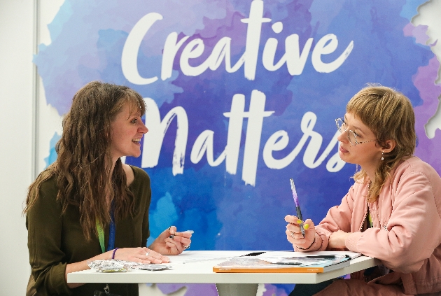 Two ladies with pens chatting informally at a table