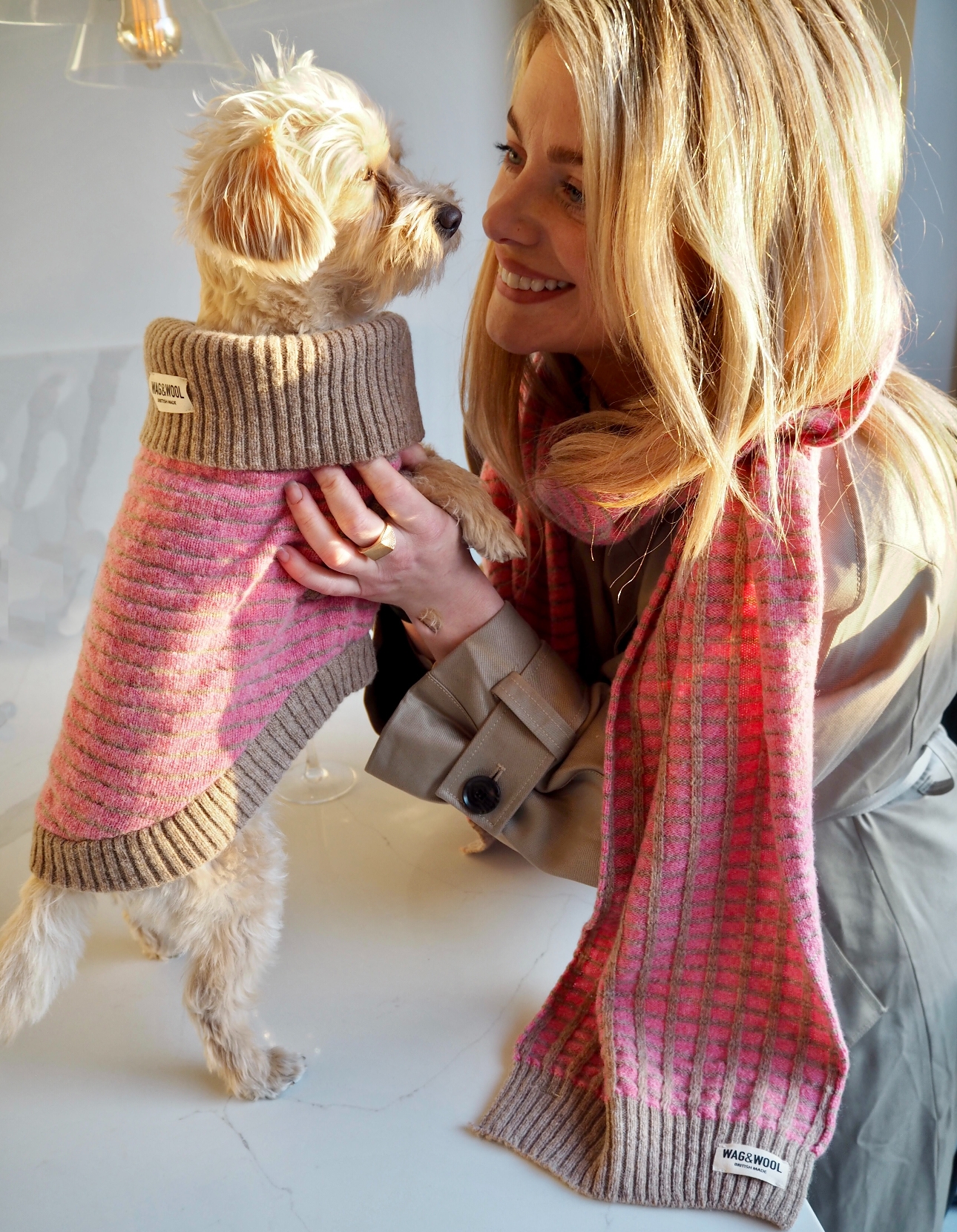 blonde woman holding dog in matching pink dog suit and scarf