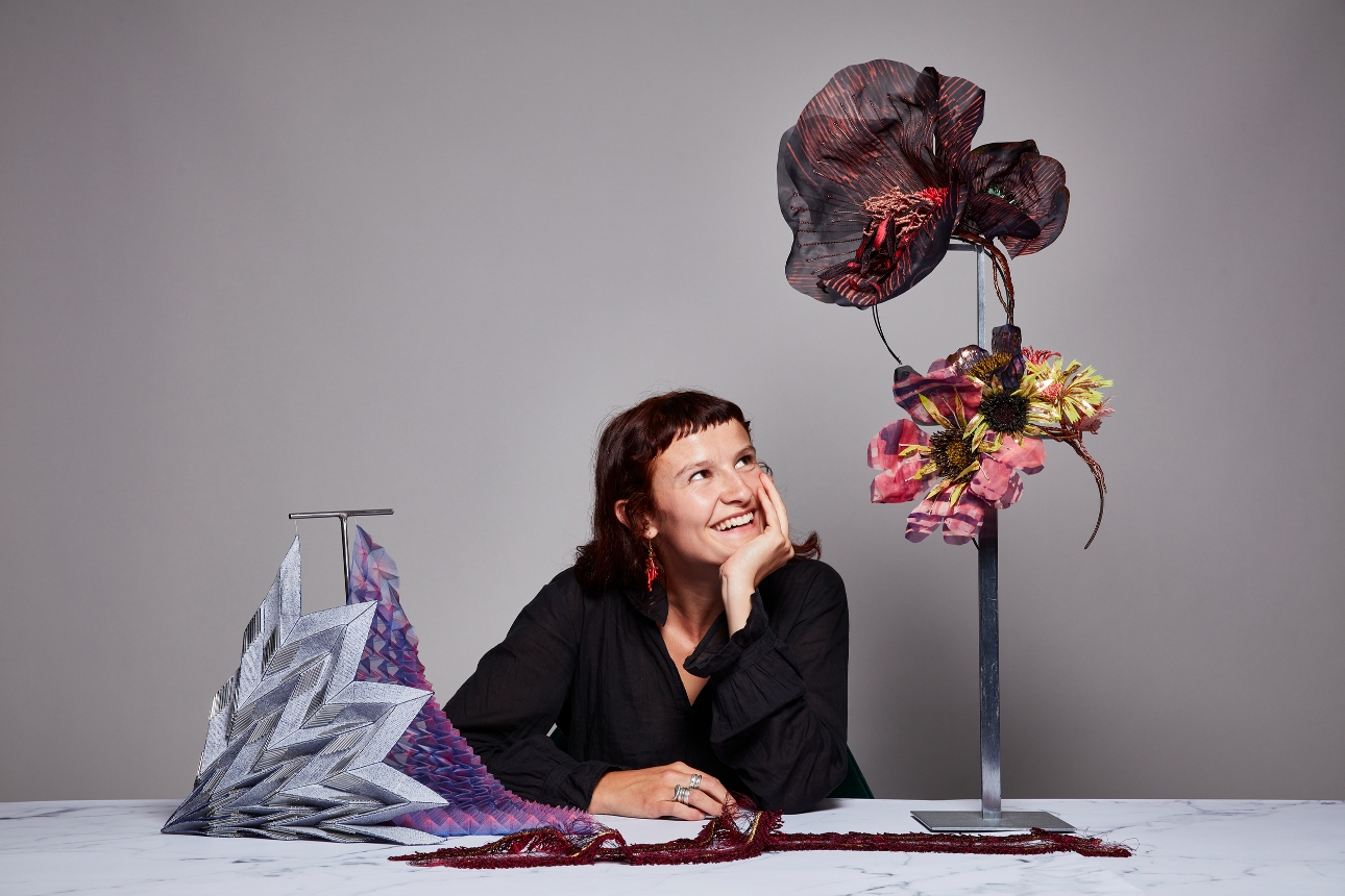 woman leaning on table looking up at a material flower