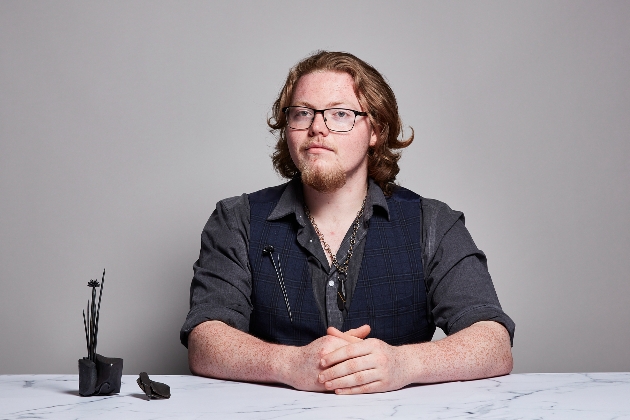 man with blonde hair and glasses sat at table with black shaped design he's made