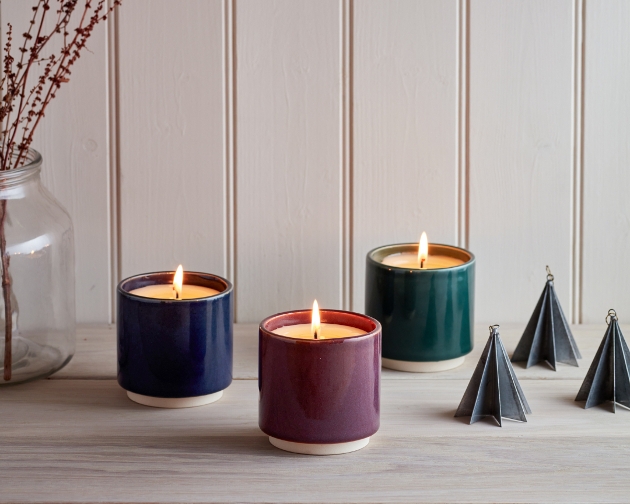 three lit candles on a shelf in dark green blue and mauve
