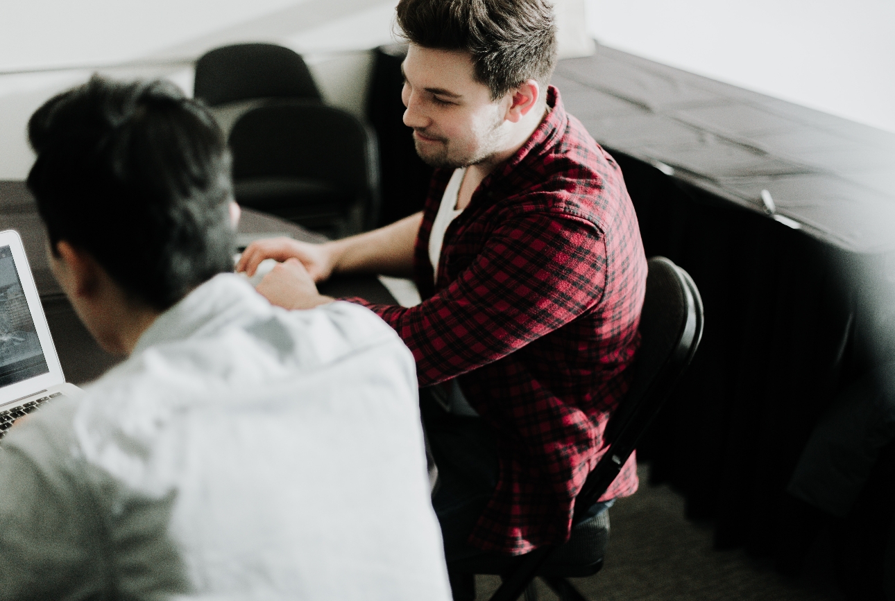 two men sat at table looking at laptop